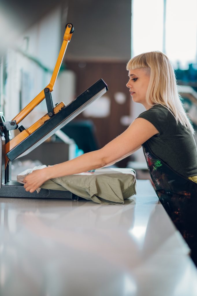 Print shop worker putting t-shirt of heating press and finishing it.