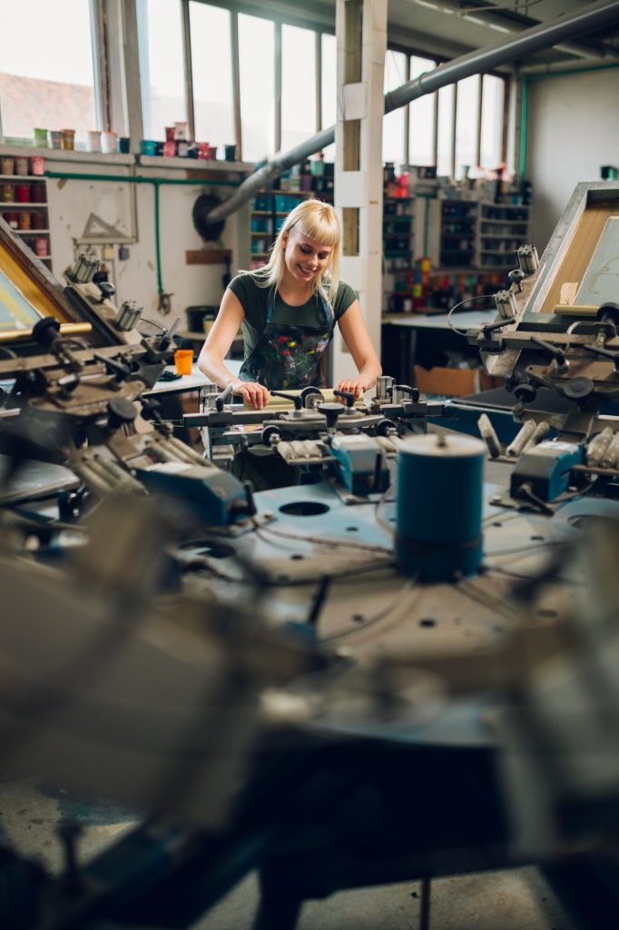 Young graphic worker is screen printing on carousel printing machine.